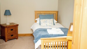 Een slaapkamer met een houten bed, een nachtkastje met een lamp en een dressoir.