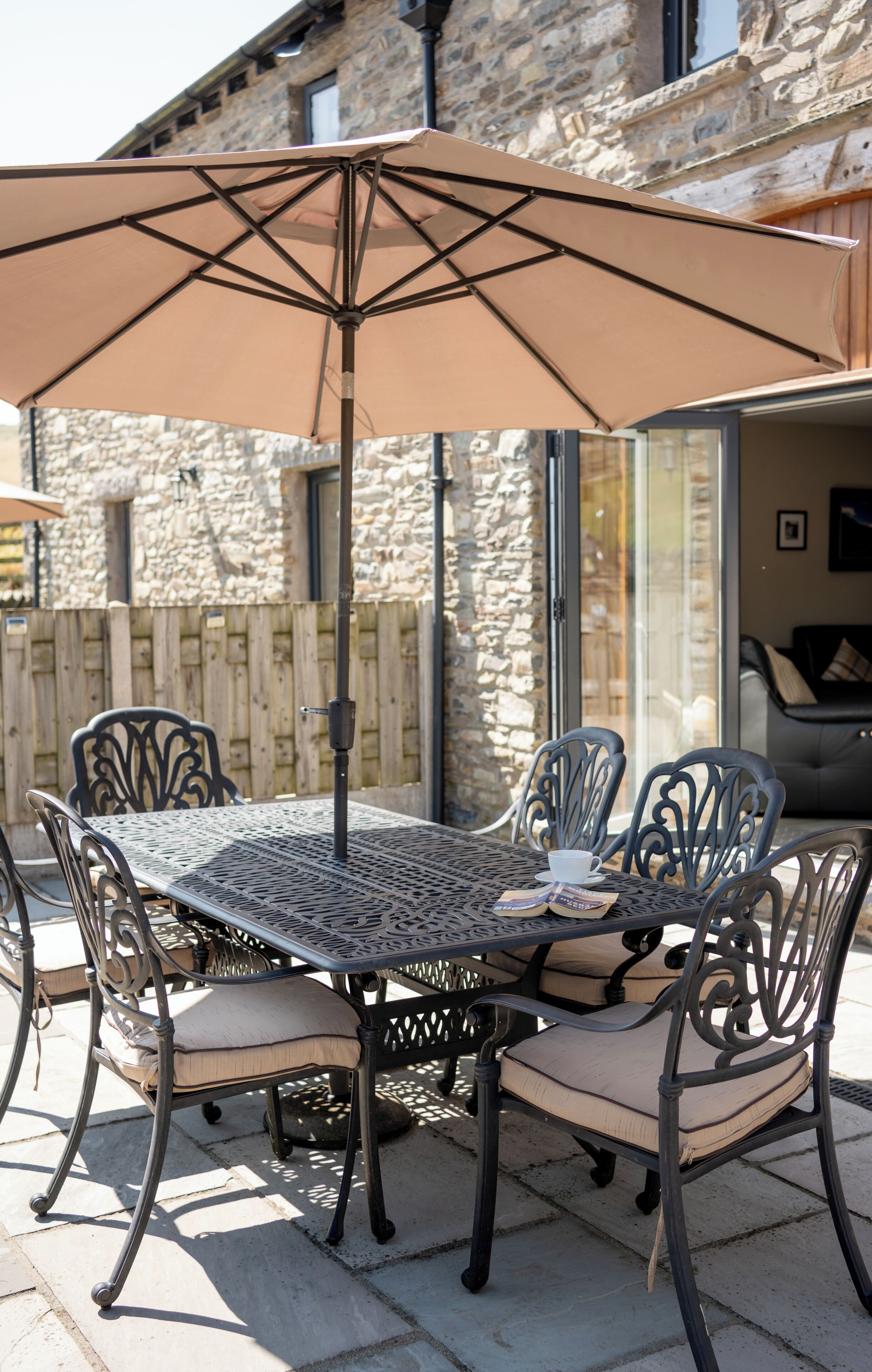 Une terrasse extérieure avec une table et des chaises en métal, un parasol et un mur de pierre en arrière-plan.