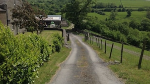A rural road with a stone bridge, surrounded by lush greenery and a farmhouse. - Stunning 3 bed cottage with exceptional views over fields and the Lakeland fells (Kendal)
