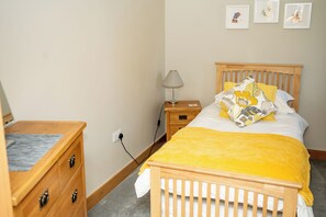 A bedroom with a wooden bed, a nightstand, a lamp, and a dresser.