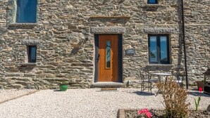 A stone cottage with a wooden door, two windows, and a small outdoor seating area with a table and chairs. - Stunning 3 bed cottage with exceptional views over fields and the Lakeland fells (Kendal)