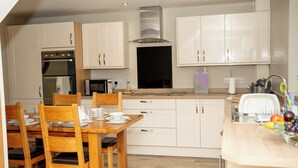 A modern kitchen with white cabinetry, a dining table with chairs, and a built-in oven. - Stunning 3 bed cottage with exceptional views over fields and the Lakeland fells (Kendal)
