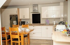 A modern kitchen with white cabinetry, a dining table with chairs, and a built-in oven.