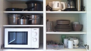 A kitchen with a microwave, pots, pans, and various kitchen utensils.