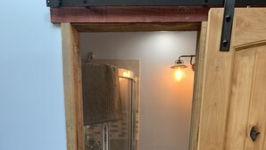 Un baño con puerta de madera, ducha con puertas de vidrio, inodoro y encimera de mármol.