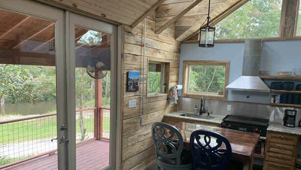 Una cabaña de madera con zona de cocina, una mesa de comedor con dos sillas y vistas al exterior a través de una puerta de cristal.
