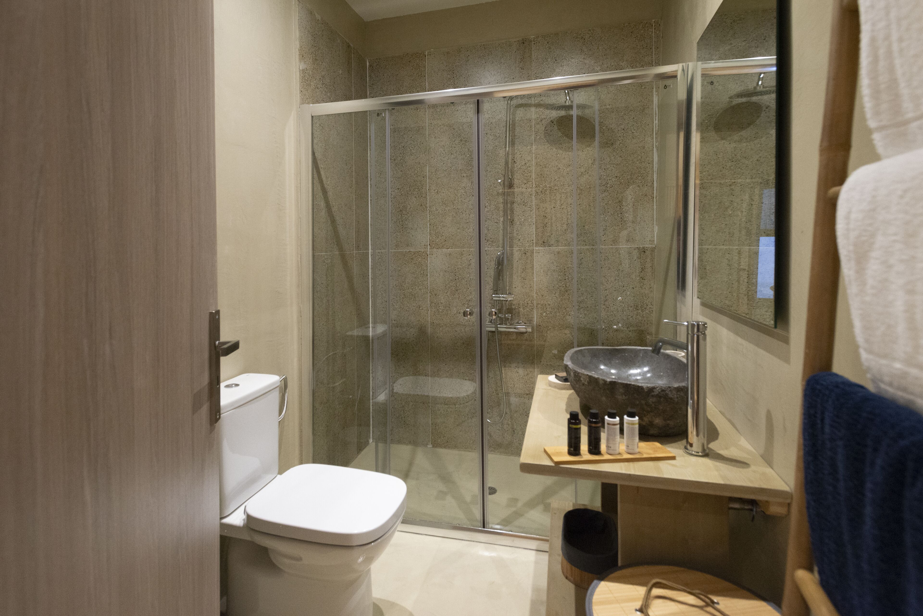 Ein modernes Badezimmer mit einer gläsernen Duschkabine, einer weißen Toilette und einem Waschbecken mit Natursteinbecken.