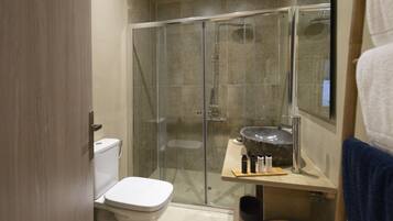 Ein modernes Badezimmer mit einer gläsernen Duschkabine, einer weißen Toilette und einem Waschbecken mit Natursteinbecken.