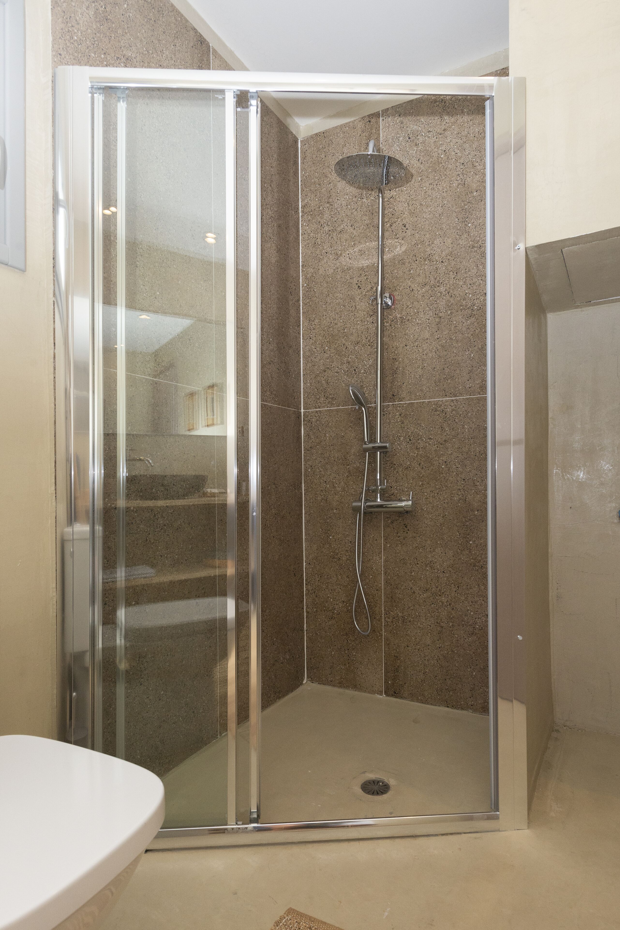 A glass-enclosed shower stall with a handheld showerhead and a wall-mounted faucet.