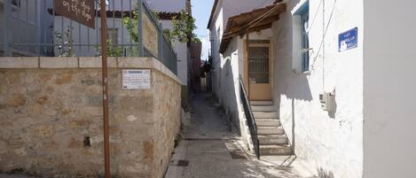 Un estrecho callejón con paredes de piedra, una reja metálica y una escalera que conduce a un edificio con un letrero azul.
