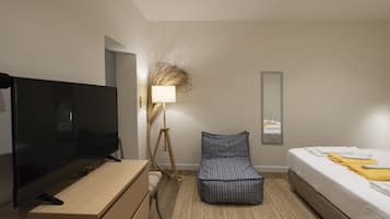 Ein modernes Hotelzimmer mit Flachbildfernseher, Nachttisch, Lampe, Sofa und einem Bett mit ordentlich drapierten Handtüchern.