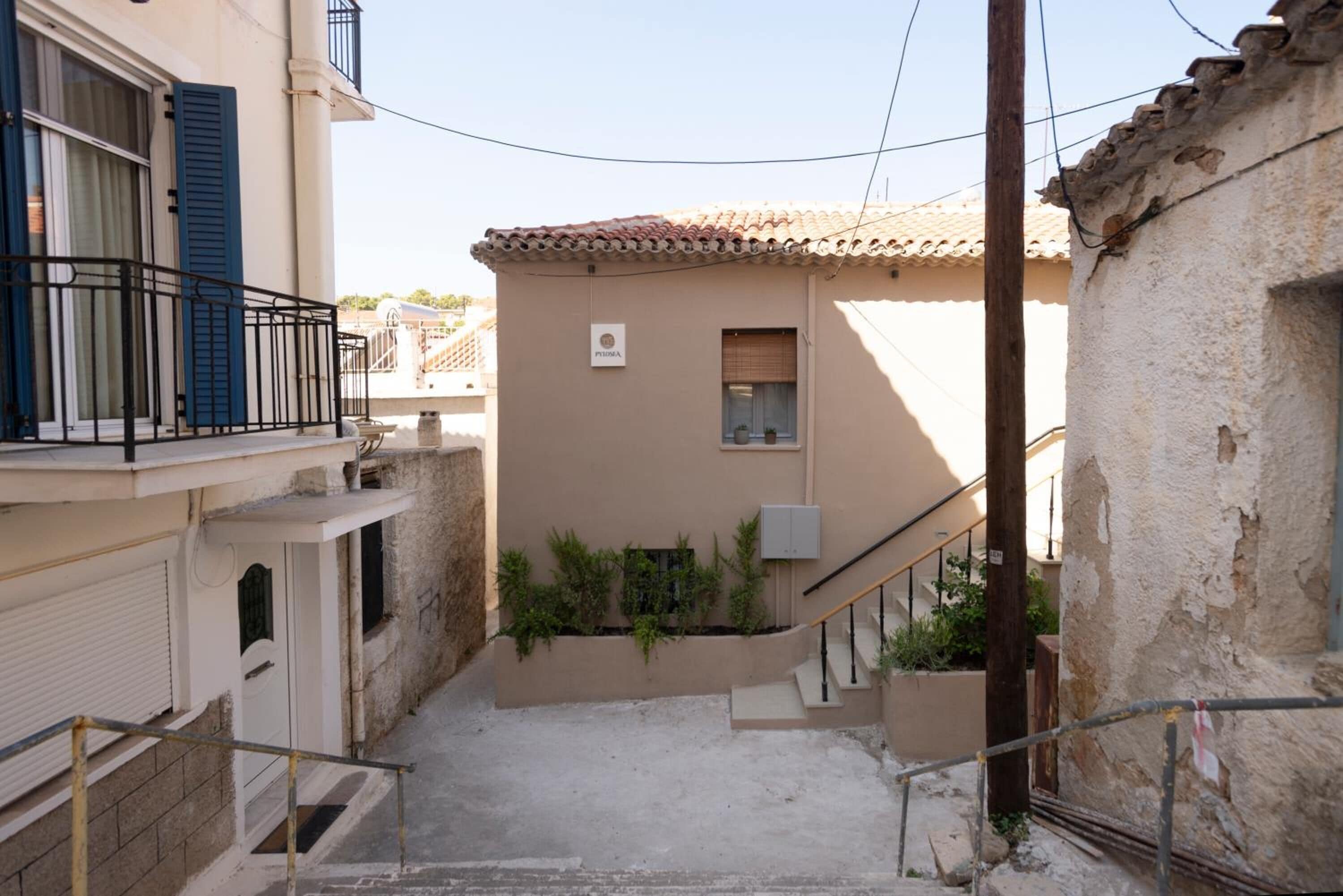 A narrow street with a building featuring a small window and a balcony with blue shutters.