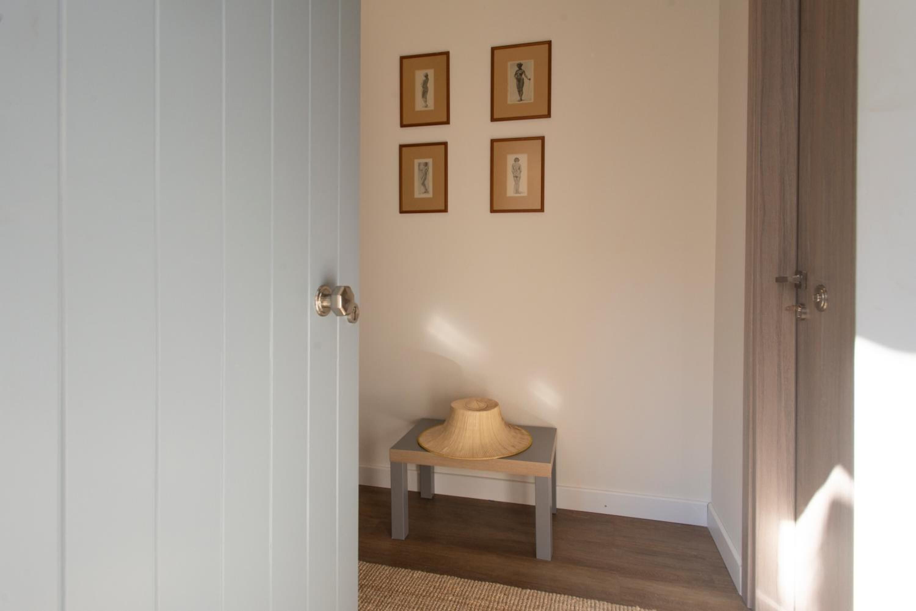 A hallway with a wooden floor, a bench with a woven basket, and four framed pictures on the wall.