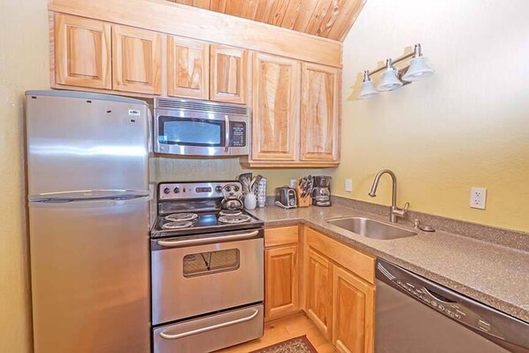 Una cocina con armarios de madera, electrodomésticos de acero inoxidable, microondas, refrigerador, lavavajillas y un lavaplatos.