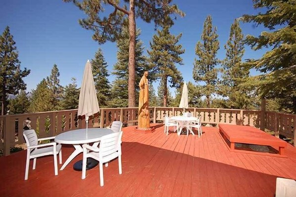 Une terrasse en bois avec un plancher rouge, des meubles d’extérieur blancs et deux parasols.