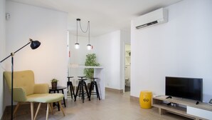 A modern living room with a sofa, a TV, a lamp, and a dining area with stools and a plant. - FLH Alfama Traditional Flat (Lisbon)