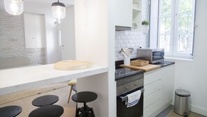 A modern kitchen with a white countertop, black stools, a wooden cutting board, and a stainless steel oven. - FLH Alfama Traditional Flat (Lisbon)