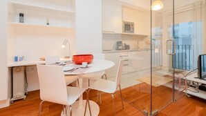 Una cuina moderna amb armaris blancs, un microones i una cafetera. Hi ha una zona de menjador amb una taula i caires blancs, i un bol vermell sobre la taula.