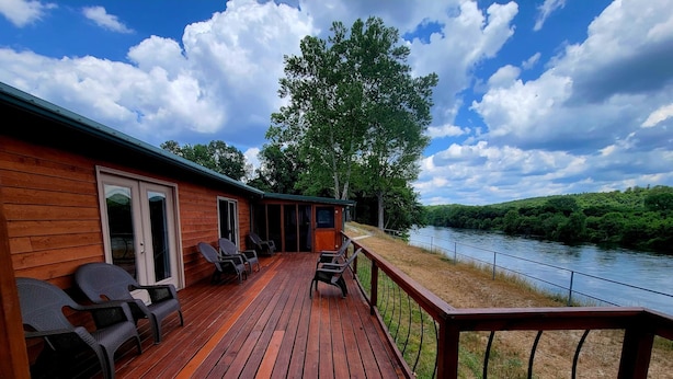 Una terraza de madera con asientos al aire libre, vista a un río y una zona cubierta con una puerta.