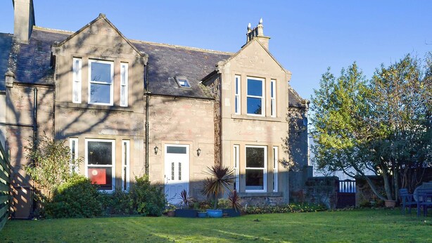 A two-story house with a well-maintained lawn, a red door, and a chimney. - 4 bedroom accommodation in Nairn (Nairn)