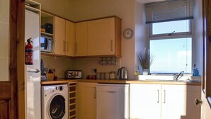 A compact kitchen with a washing machine, dishwasher, and wooden cabinets. - 4 bedroom accommodation in Nairn (Nairn)
