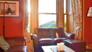 A room with a brown leather sofa, a wooden coffee table with candles, and a framed picture on the wall. - 4 bedroom accommodation in Nairn (Nairn)