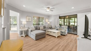A living room with a grey sofa, a white coffee table, a patterned armchair, and a flat-screen TV. - Golf Cart ~ Screened Patio ~ Golf Course Views (Miramar Beach)