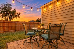 Une terrasse extérieure avec une table et des chaises, une clôture en bois et des guirlandes lumineuses.