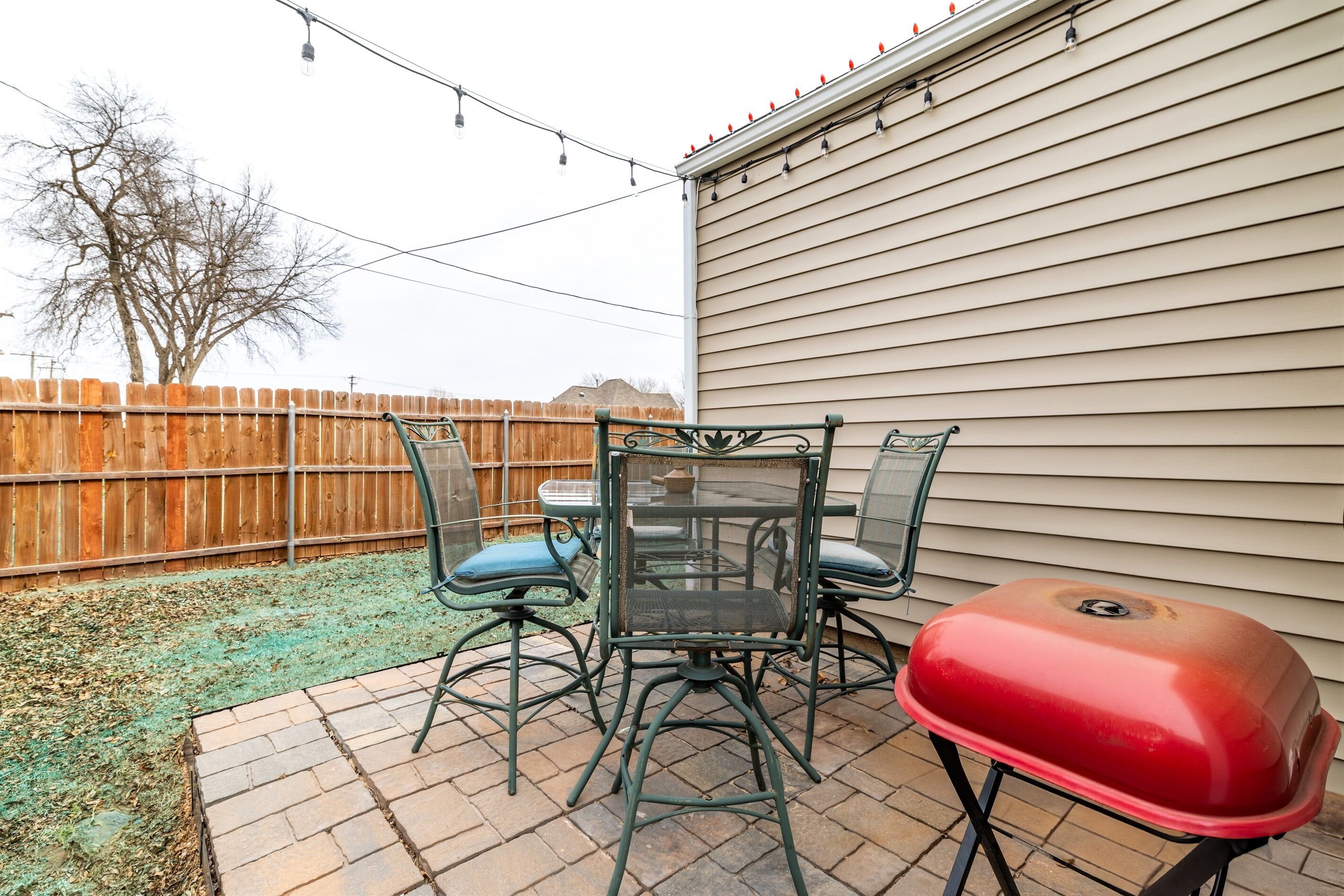 A patio with a table and chairs, a barbecue grill, and a wooden fence.