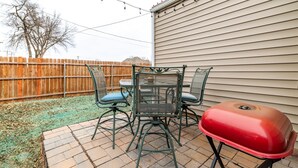 Une terrasse avec une table et des chaises, un barbecue et une clôture en bois.
