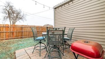 A patio with a table and chairs, a barbecue grill, and a wooden fence.