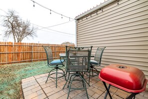 A patio with a table and chairs, a barbecue grill, and a wooden fence.