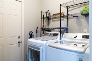 Un espace buanderie comprenant un lave-linge et un sèche-linge, une étagère en métal avec des produits de nettoyage et une porte.