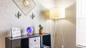 Une pièce avec un mur à texture, une console en bois foncé dotée de rangements, un lampadaire, un cactus, une petite plante en pot et un panneau indiquant la disponibilité du Wi-Fi.