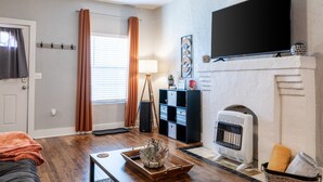 A living room with hardwood flooring, a fireplace, a mounted TV, and a modern fireplace mantel. - The Cozy Chickasha | Fiber | Extra Parking | W/D (Chickasha)