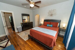 Une chambre à coucher comprenant un lit, une commode, un miroir, un ventilateur de plafond et un tapis.