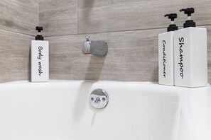 A bathroom with a bathtub, two bottles of body wash, and two bottles of shampoo.