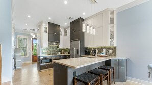 Une cuisine moderne dotée d’un grand îlot central, de tabourets de bar, d’appareils électroménagers en acier inoxydable et de luminaires suspendus.