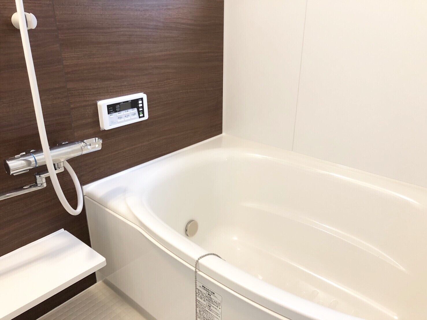 A modern bathroom with a white bathtub, a digital control panel, and a wooden wall.