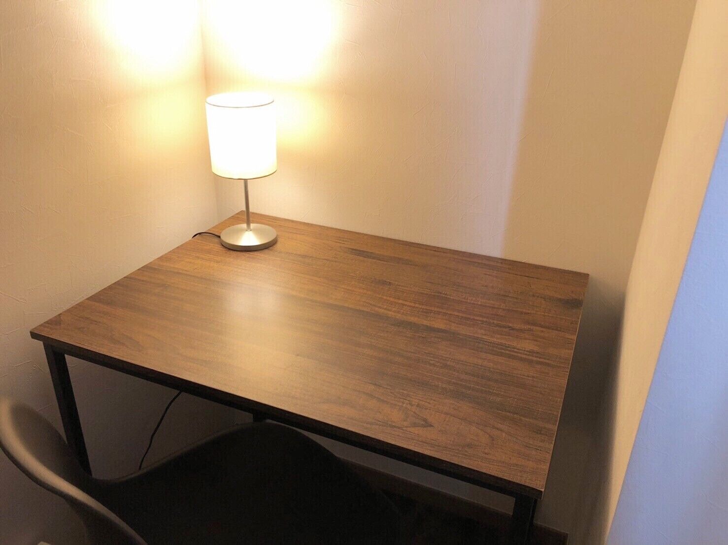 Una pequeña mesa de madera con una lámpara, ubicada junto a una pared.