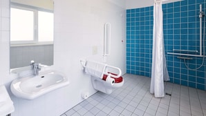 Et badeværelse med en hvid vask, et toilet med gelænder, en bruseniche med blå fliser og et vindue.
