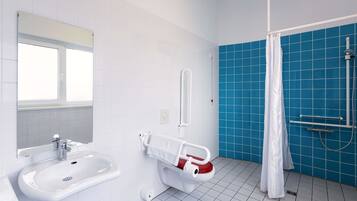 Ein Badezimmer mit weißem Waschbecken, einer Toilette mit Handlauf, einer Dusche mit blauen Fliesen und einem Fenster.