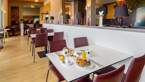 Et moderne spiseområde med flere borde og stole, en disk med kaffemaskine, og forskellige morgenmadsretter på bordene.