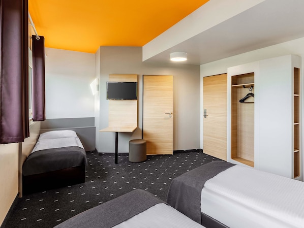 Hotellihuone, jossa on kaksi sänkyä, seinälle asennettu televisio, puinen vaatekaappi ja pieni pöytä.