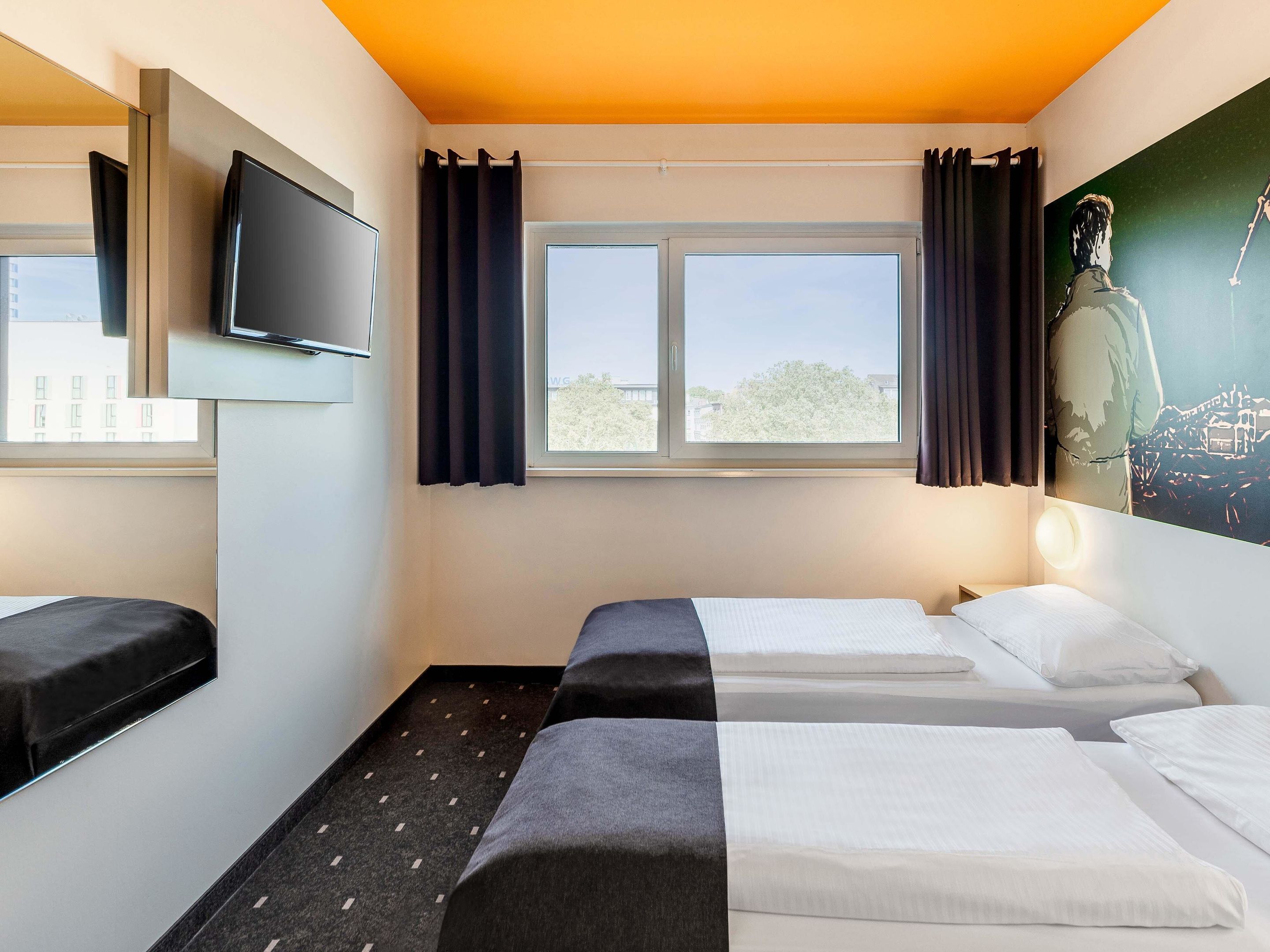 Ein Hotelzimmer mit zwei Betten, einem Fernseher und einem Fenster mit Vorhängen.
