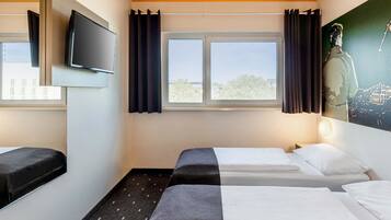 Ein Hotelzimmer mit zwei Betten, einem Fernseher und einem Fenster mit Vorhängen.