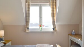 Una camera da letto con un letto, una scrivania, una finestra con tende e vista sul mare.
