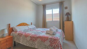 A neatly made bed with a floral bedspread, a bedside lamp, and a wooden nightstand. - 040 - Gran Playa 001 - Santa Pola (Santa Pola)