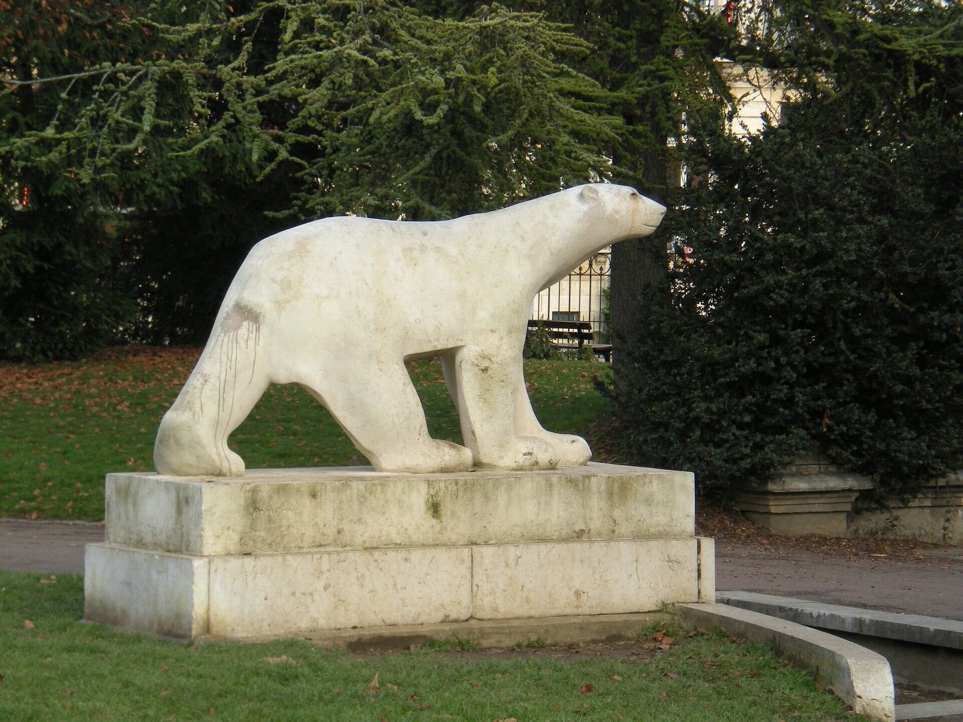 A polar bear statue on a concrete pedestal in a park.