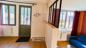 Una habitación con piso de madera, un sofá azul, una puerta con picaporte negro y una ventana con vista a edificios.
